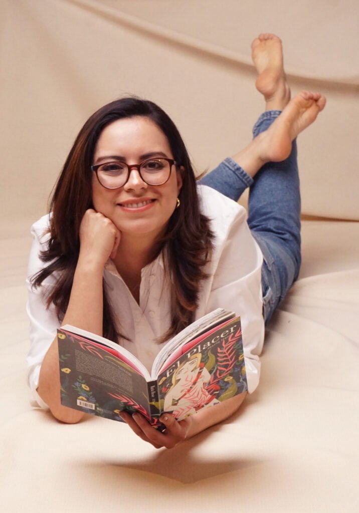 Karla Iris recostada leyendo un libro, sonriendo a cámara